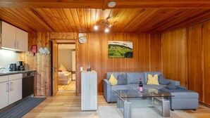 A wooden interior with a sofa, coffee table, and a kitchen area. - Two modern holiday flats on the farm, ski-out (Itter)