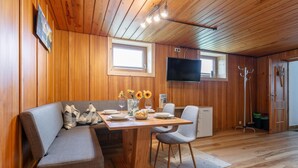 A cozy room with a wooden ceiling, a dining table set for two, a sofa, and a TV mounted on the wall. - Two modern holiday flats on the farm, ski-out (Itter)