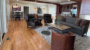 A spacious living room with a wooden floor, a large sofa, two armchairs, a coffee table, and a dining area with a table and chairs. - NEW-Skaneateles Level Lakefront-Ready to Rent! (Skaneateles)