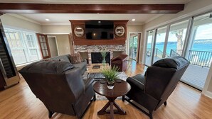 A spacious living room with a fireplace, leather sofas, and a view of the sea. - NEW-Skaneateles Level Lakefront-Ready to Rent! (Skaneateles)