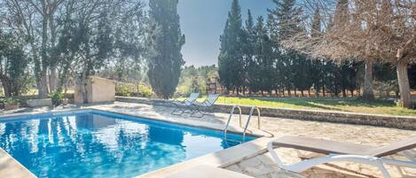 A swimming pool with lounge chairs, surrounded by trees and a stone wall.