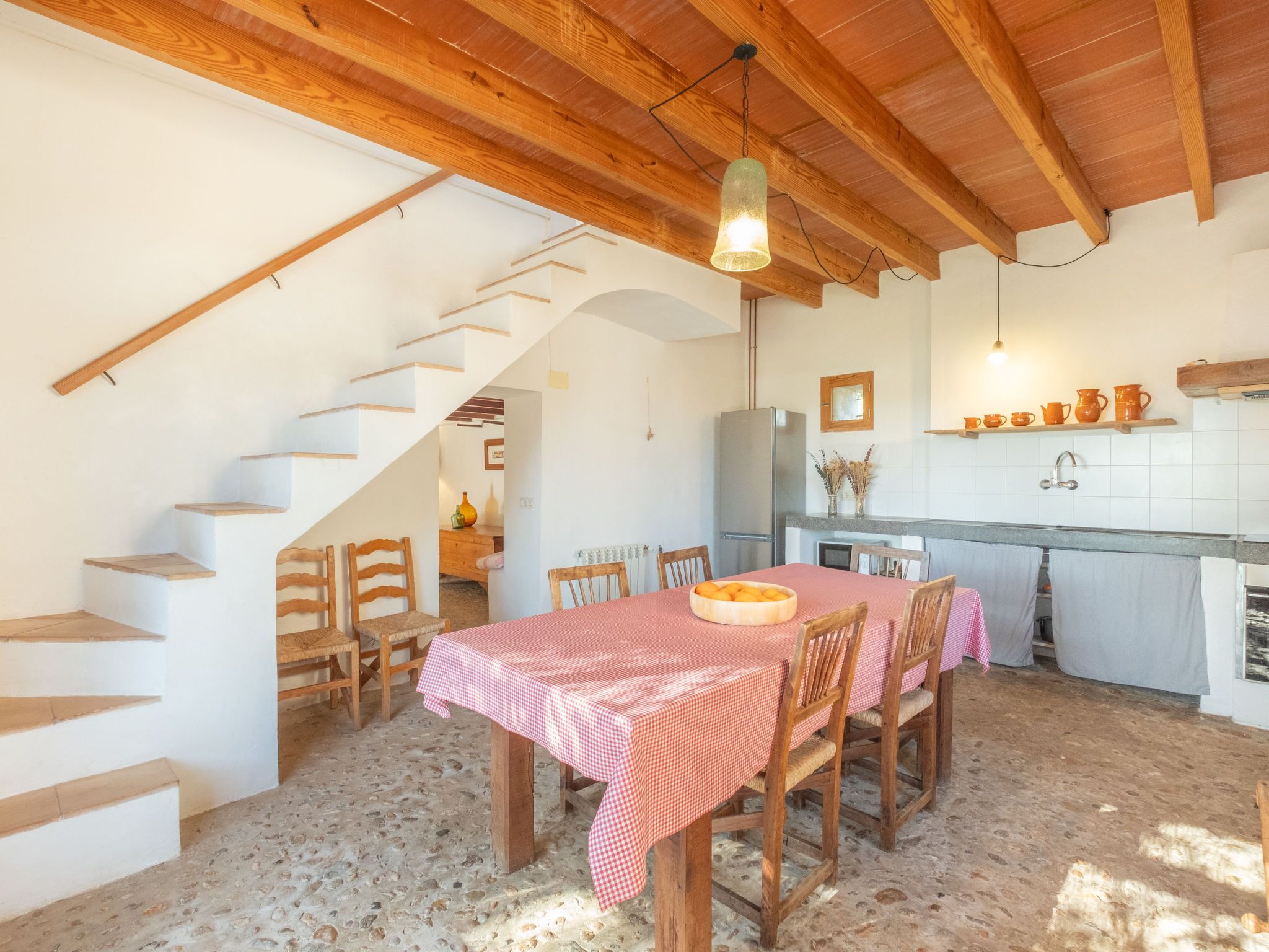 Una cocina rústica con una escalera de madera, una mesa de comedor con sillas y un refrigerador.
