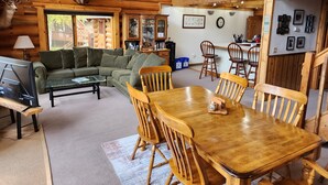 Un interior de cabaña acogedor, con una mesa de comedor de madera, sillas, un sofá y una televisión.