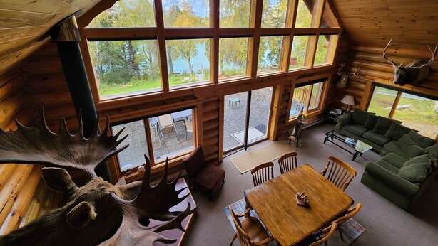 Una cabaña con amplias ventanas, interior de madera, comedor y sofá verde.