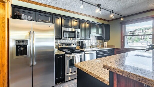 A modern kitchen with stainless steel appliances, dark cabinetry, and a granite countertop.