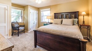 A bedroom with a dark wooden bed, beige walls, a ceiling fan, and a window with blinds.
