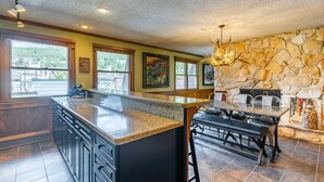 A kitchen with a large island, stone wall, and a dining area with a bench.