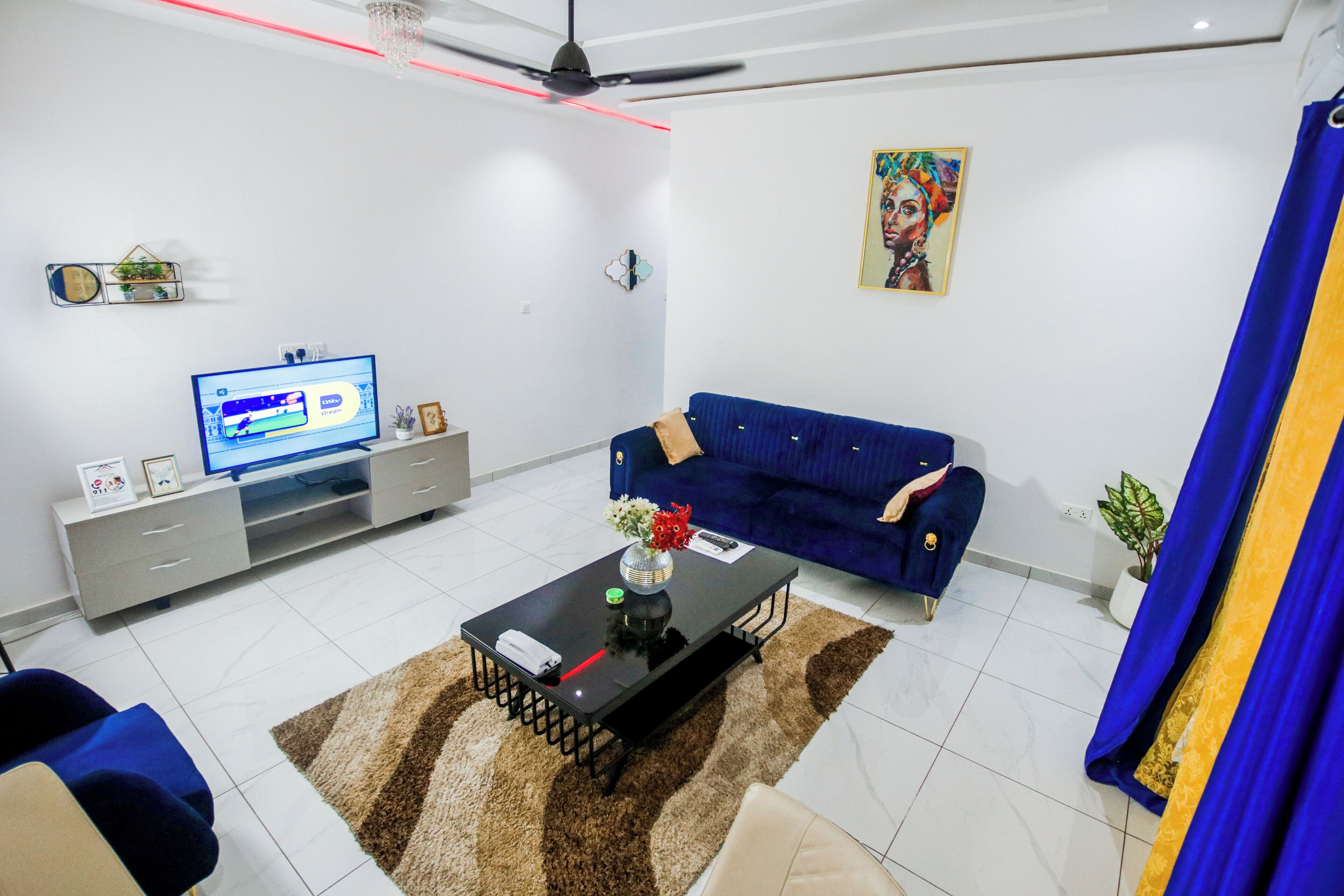 Ein modernes Wohnzimmer mit Flachbildfernseher, einem blauen Sofa, einem Couchtisch und einem Deckenventilator.