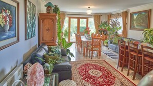 A spacious living room with a sofa, dining table, and chairs, surrounded by various plants and artwork. - Cosy retreat with spectacular mountain views, central to Kaikoura's attractions  (Hapuku)