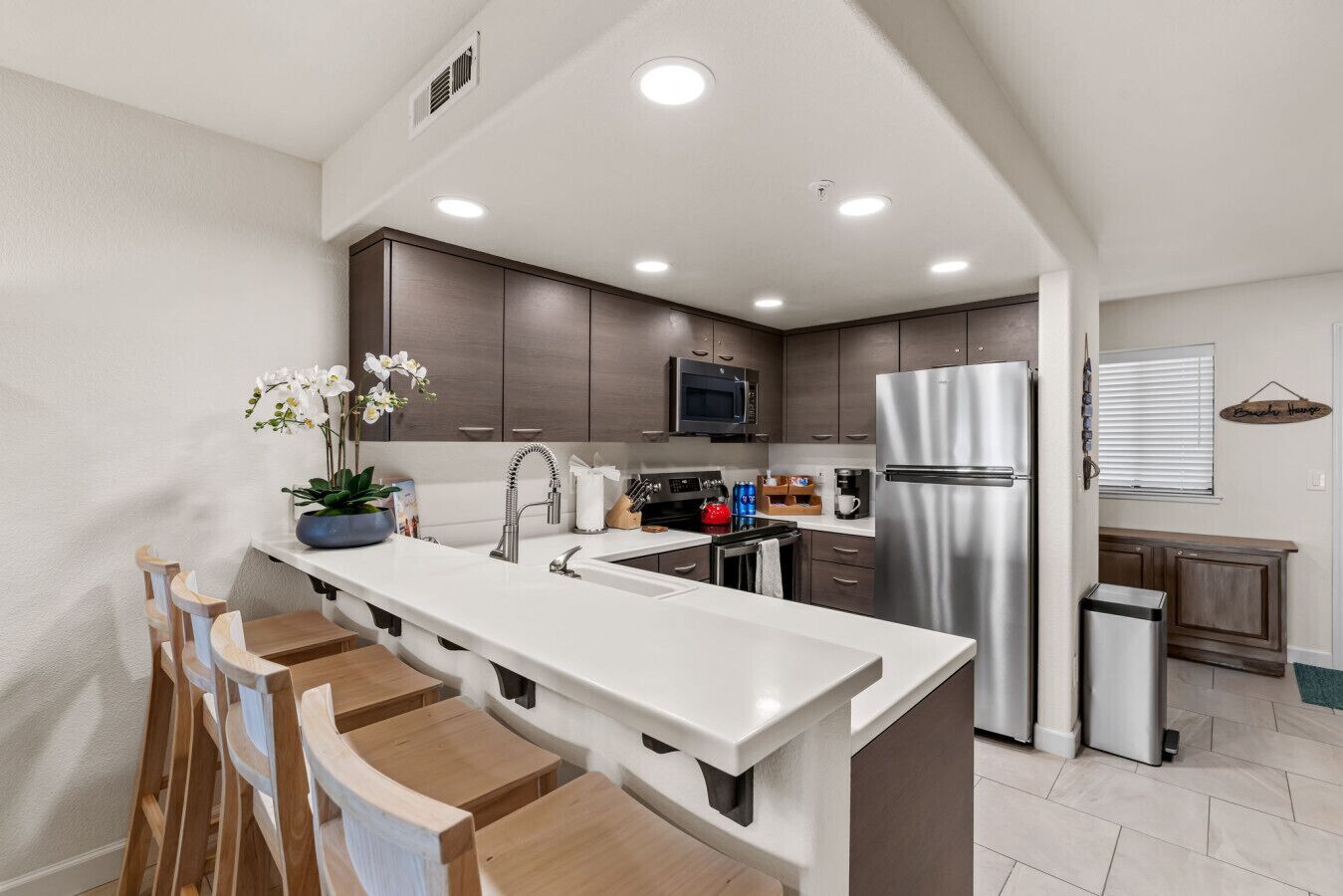 A modern kitchen with a central island, stainless steel appliances, and wooden chairs.