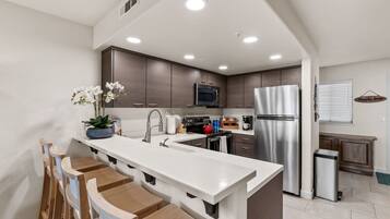 A modern kitchen with a central island, stainless steel appliances, and wooden chairs.