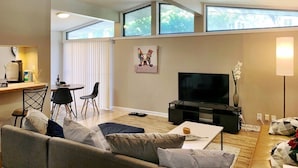 A modern living room with a sofa, coffee table, TV, and dining area. - Amazing and centrally located summer oasis with a Mid-century modern feel (Austin)