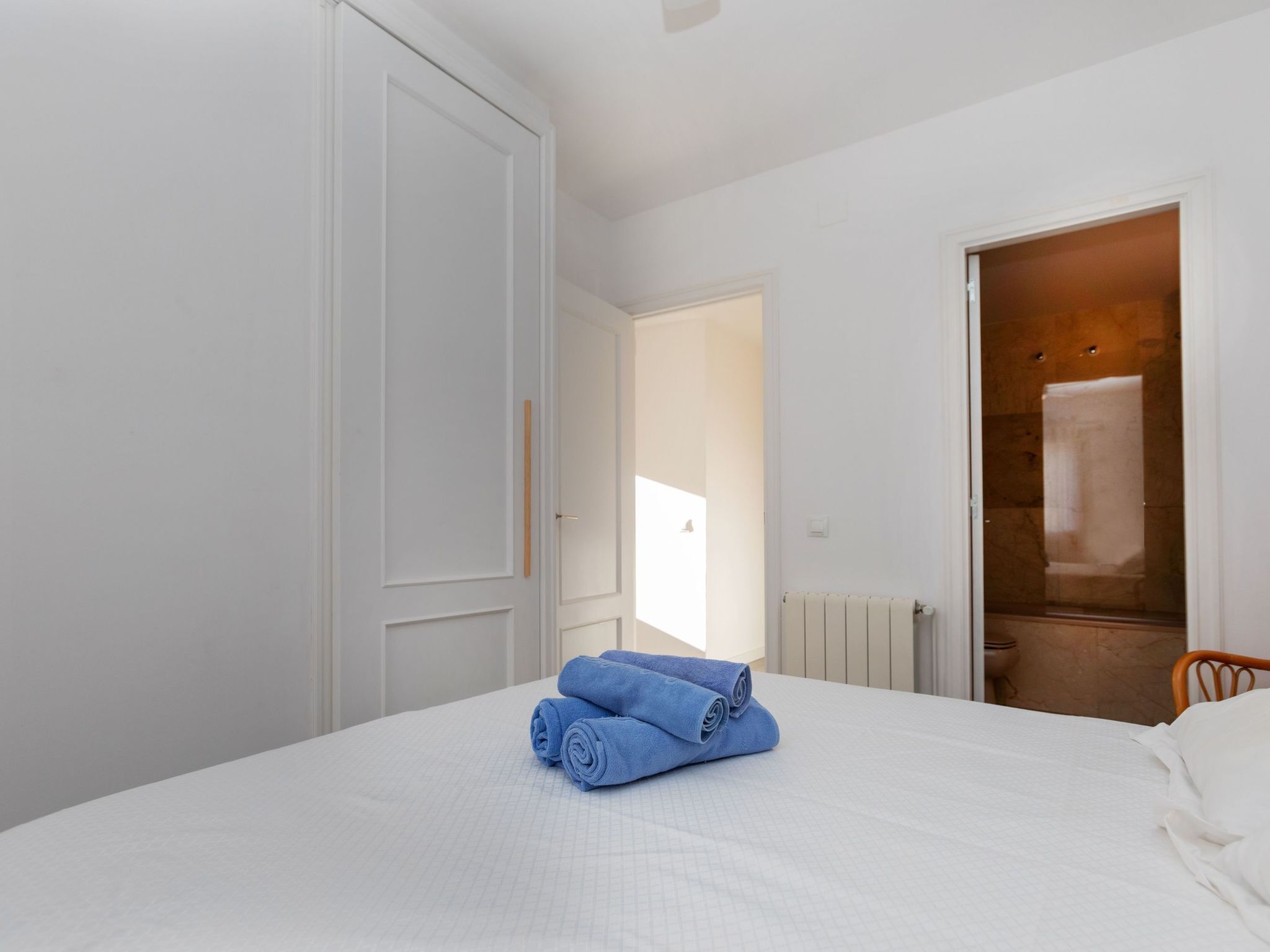 Un dormitorio con una cama grande, una silla de madera y un baño visible a través de una puerta abierta.