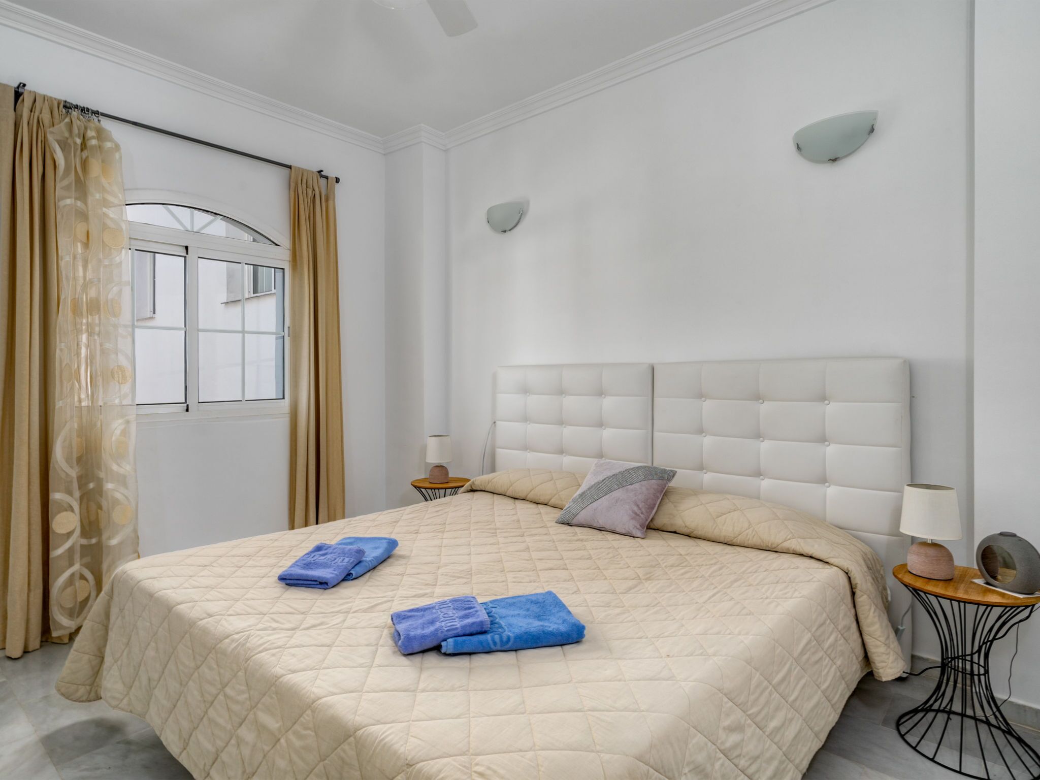 Een hotelkamer met een groot bed, twee nachtkastjes, een raam met gordijnen en een wandlamp.