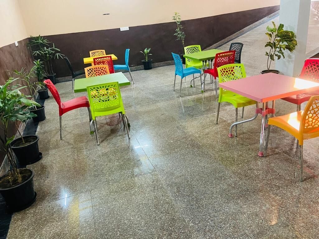 Un'ampia area interna con diversi tavoli e sedie, alcune con struttura in metallo e altre in plastica. Piante in vaso disposte intorno ai tavoli.