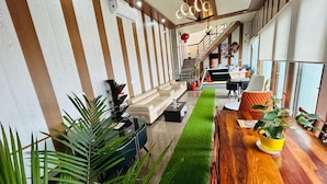 A modern living room with a wooden dining table, green artificial grass, and potted plants. - Cohouse (Bawal)