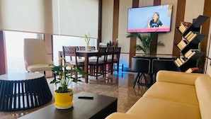 A modern living room with a sofa, a coffee table with a plant, a TV mounted on the wall, and a bookshelf. - Cohouse (Bawal)