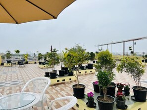 A rooftop terrace with potted plants, white wicker chairs, and a glass table. - Cohouse (Bawal)