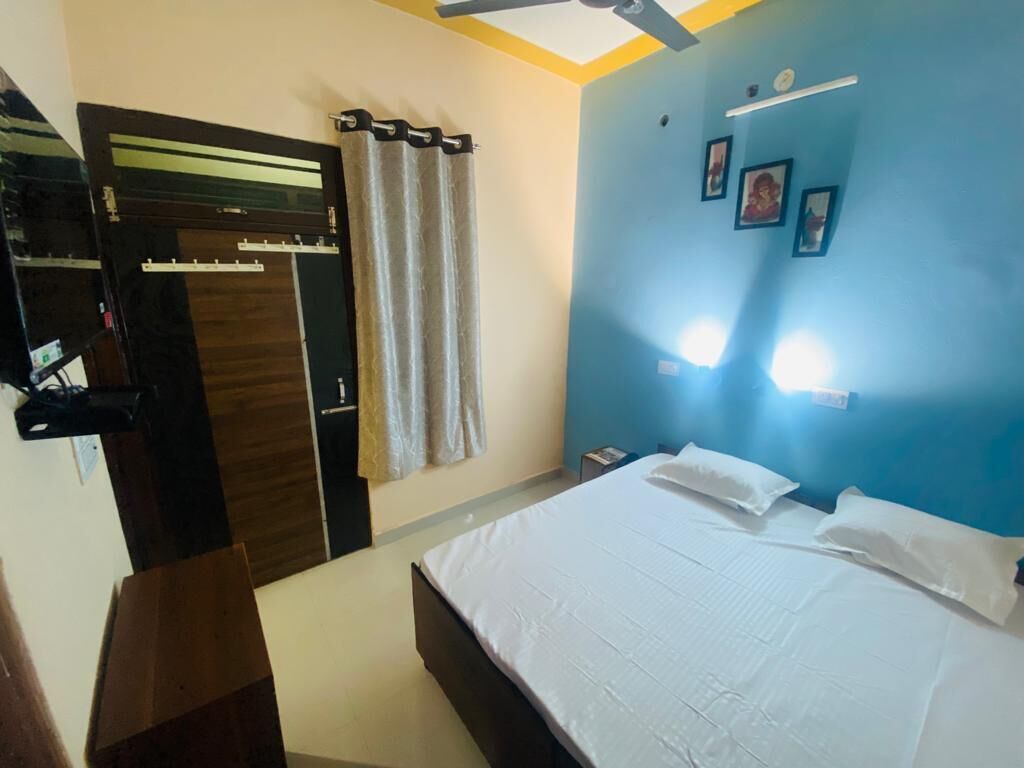 Quarto com cama, guarda-roupa, ventoinha no teto e prateleira na parede com quadros.