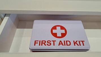 A white first aid kit with a red cross symbol and the text "FIRST AID KIT" on a white shelf.