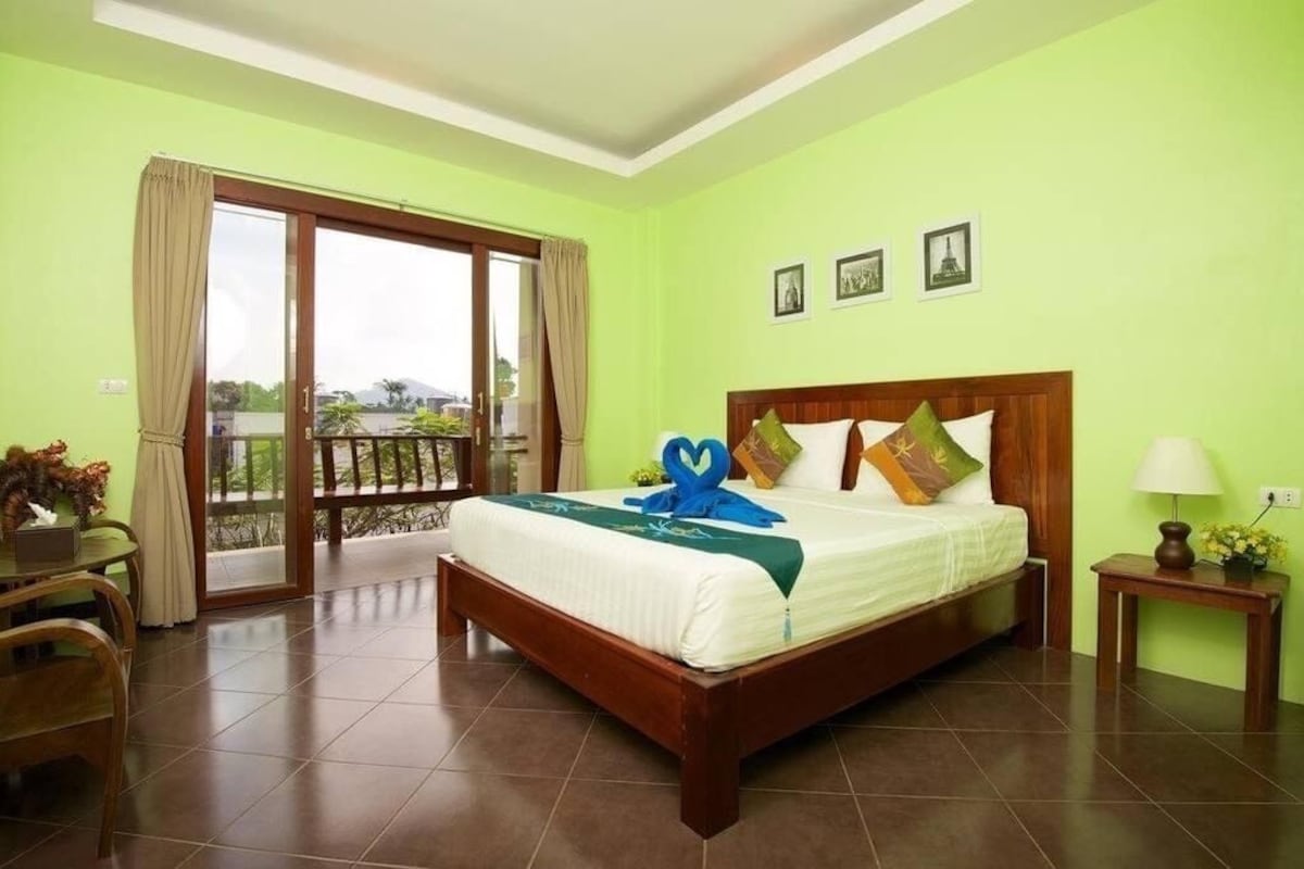 A hotel room with a bed, a desk, a chair, a nightstand, and a view of the outdoors.