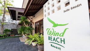 A sign for Wind Beach Resort with a bird logo, surrounded by potted plants and a building entrance. - Wind Beach Resort (Koh Tao)