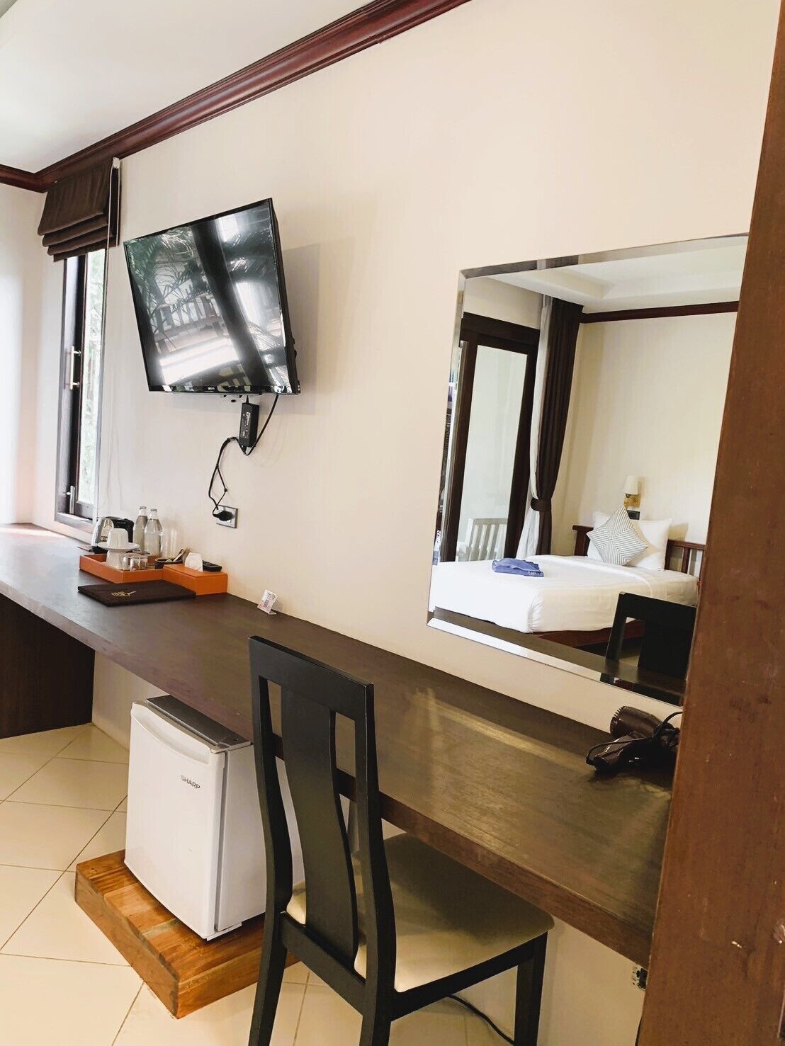 Una habitación de hotel con cama, escritorio con computadora, televisión y refrigerador pequeño.