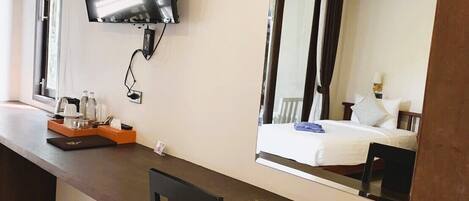 Una habitación de hotel con cama, escritorio con computadora, televisión y refrigerador pequeño.