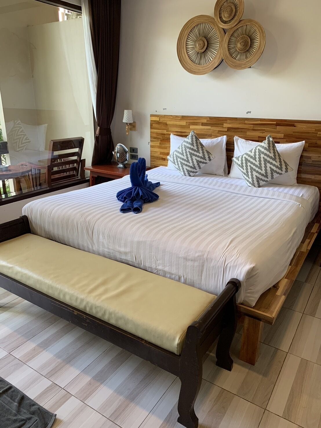 A neatly made bed with a bench, a wooden headboard, and decorative wall art.
