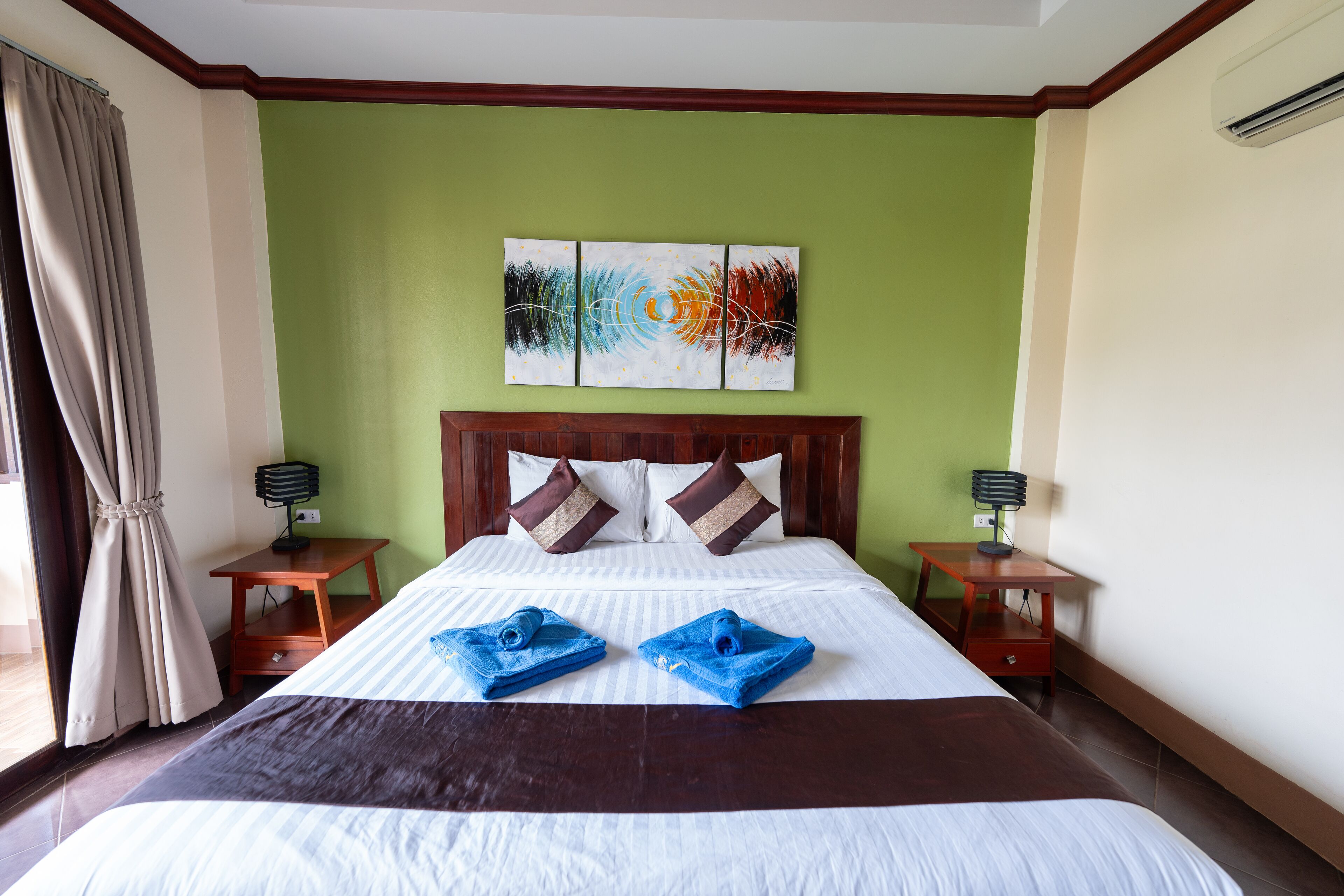 Une chambre d’hôtel avec un grand lit, des murs verts, un ventilateur de plafond et un tableau au-dessus du lit.