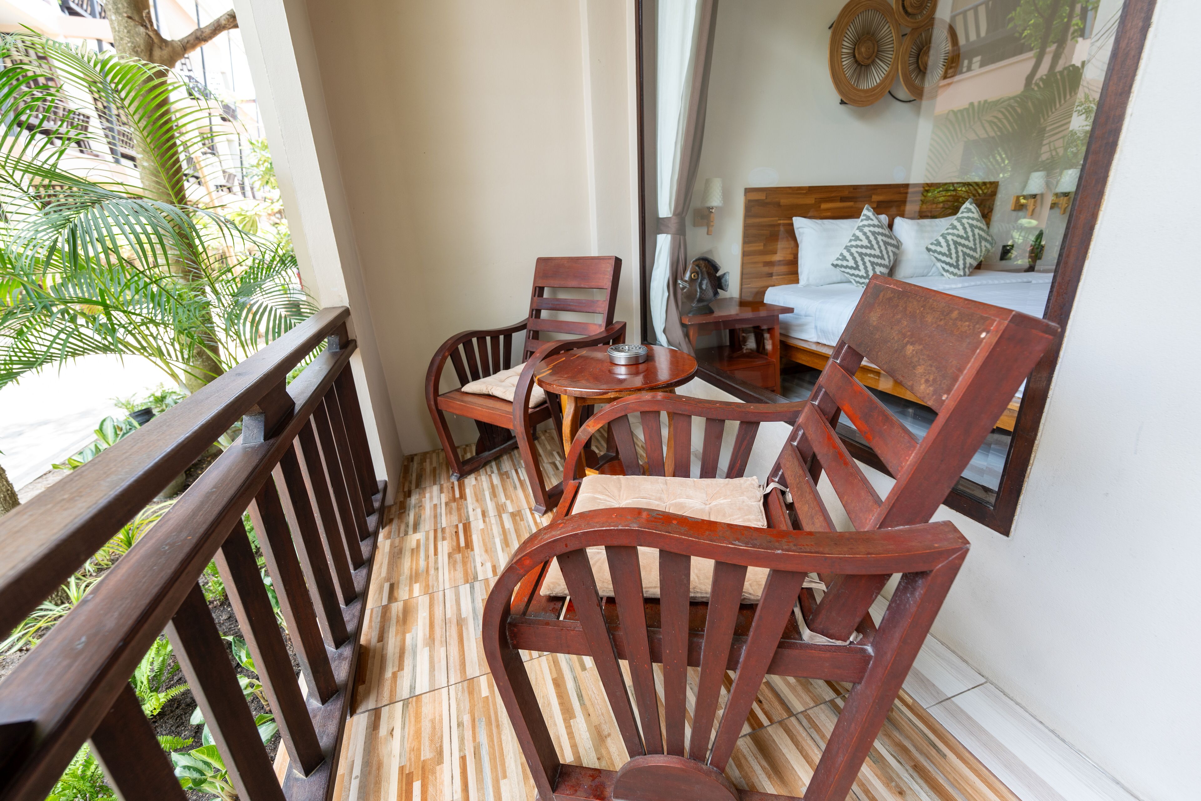 Un balcon avec des chaises en bois et une petite table, donnant sur un jardin planté de palmiers.