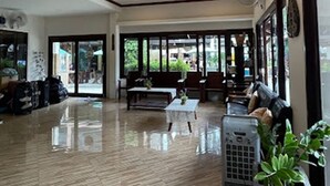 A spacious lobby with a polished floor, seating area with sofas and tables, large windows, and a visible air conditioning unit. - Wind Beach Resort (Koh Tao)
