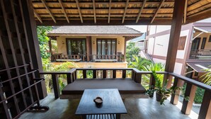 A covered outdoor seating area with a table and benches, surrounded by plants and overlooking a building with a balcony. - Wind Beach Resort (Koh Tao)