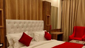 A hotel room with a large bed, wooden paneling on the walls, a red chair, and a small table. - Hotel Grand Hill (Dharamshala)
