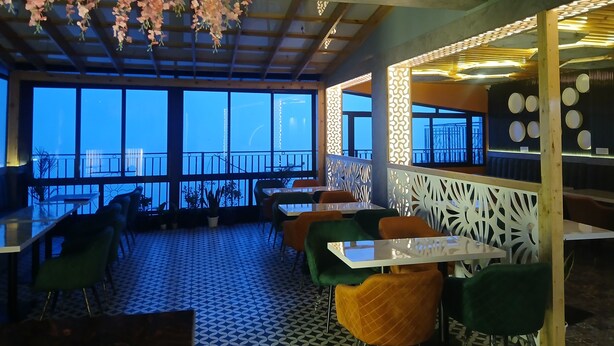 A restaurant with large windows, indoor plants, and a patterned floor. - Hotel Grand Hill (Dharamshala)