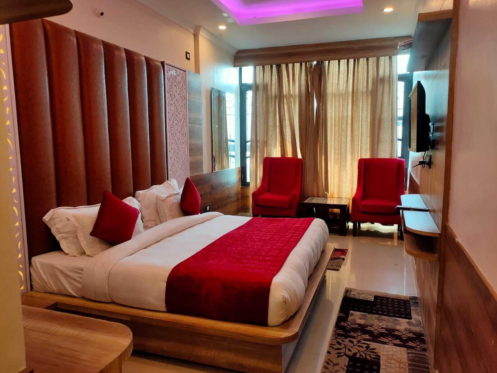A hotel room with a large bed, two red armchairs, a small table, and a TV.