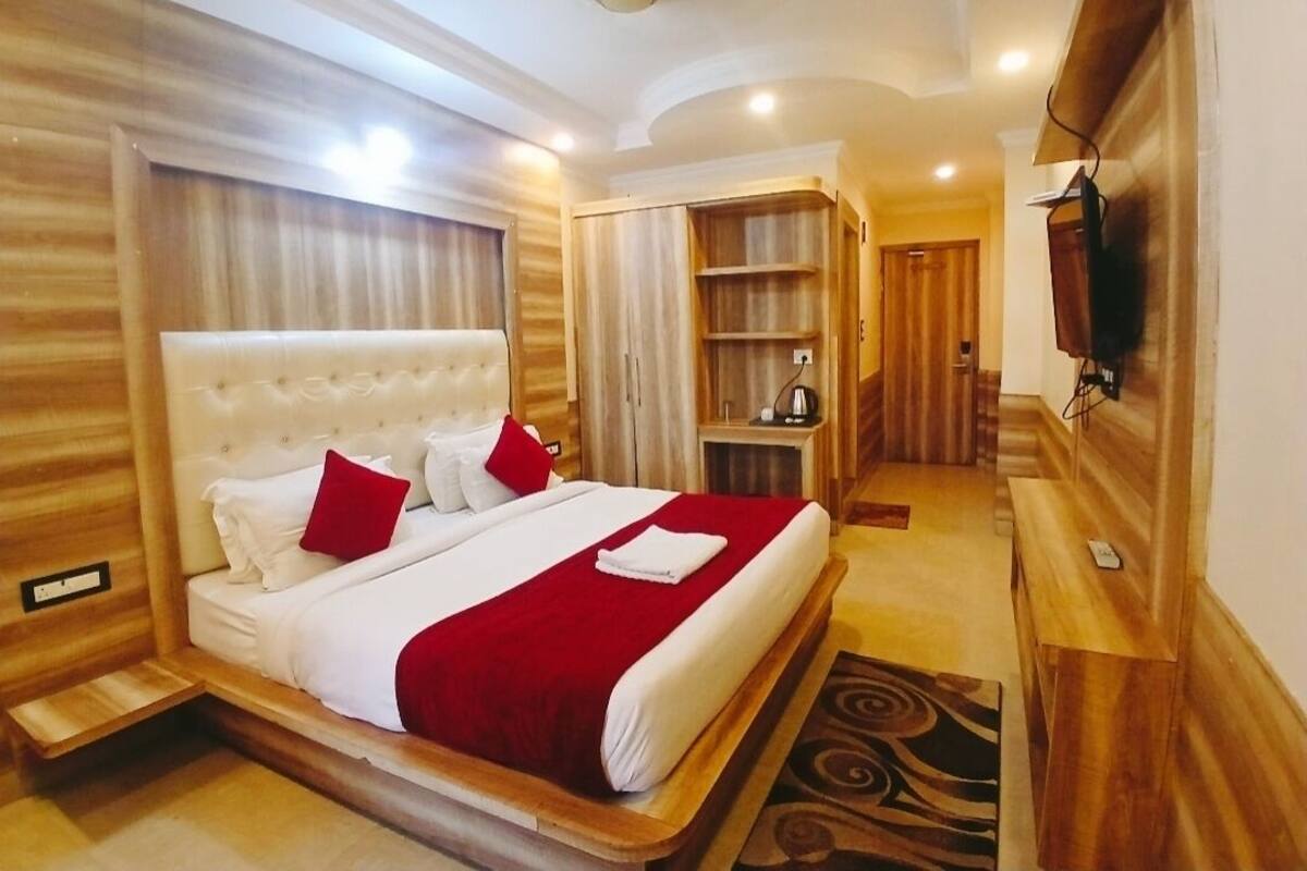 Ein Hotelzimmer mit einem großen Bett, einem Holz-Kopfteil, einem an der Wand montierten Fernseher und einem eingebauten Kleiderschrank.