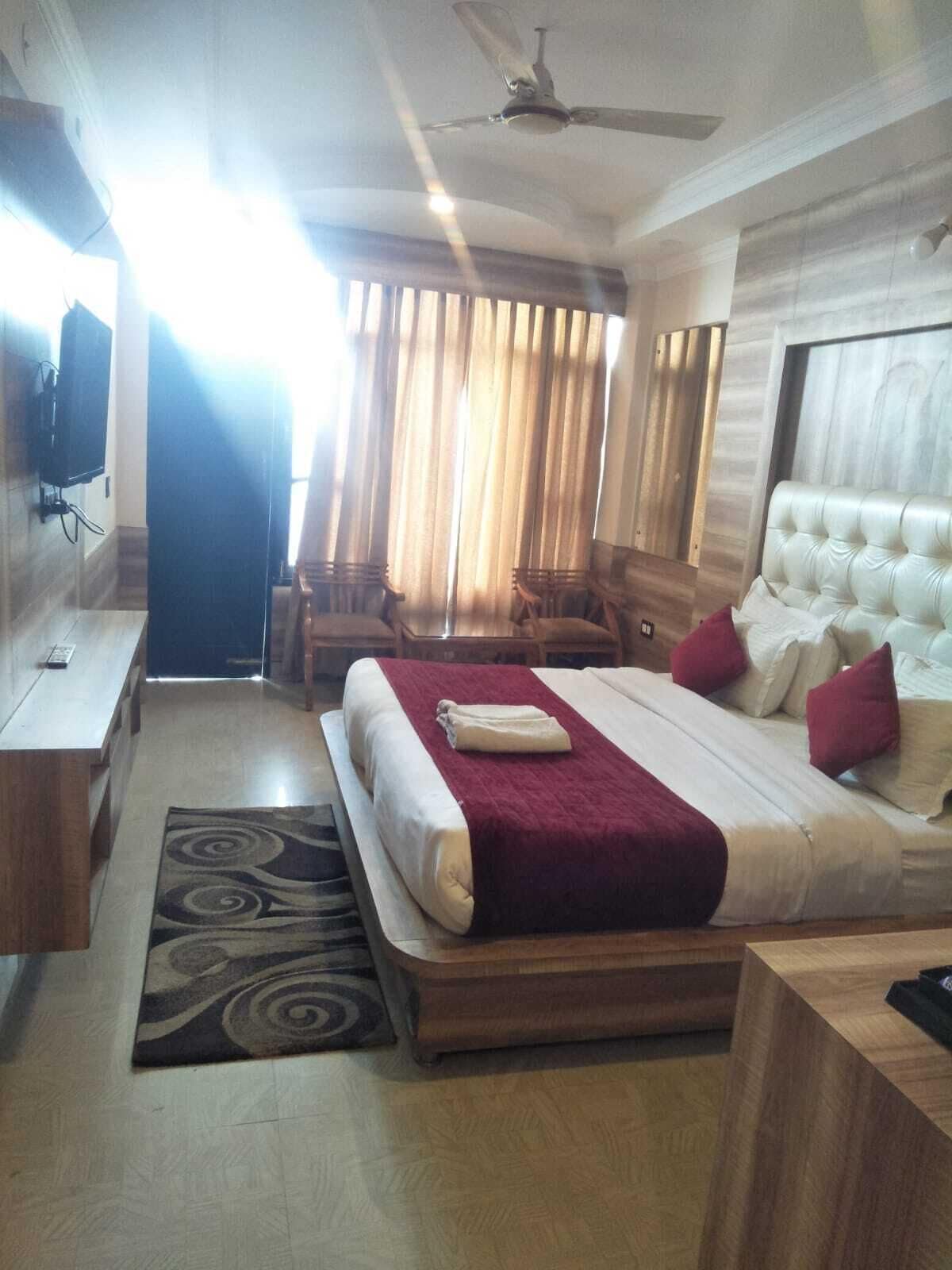 A hotel room with a bed, a TV, a ceiling fan, and a window with curtains.