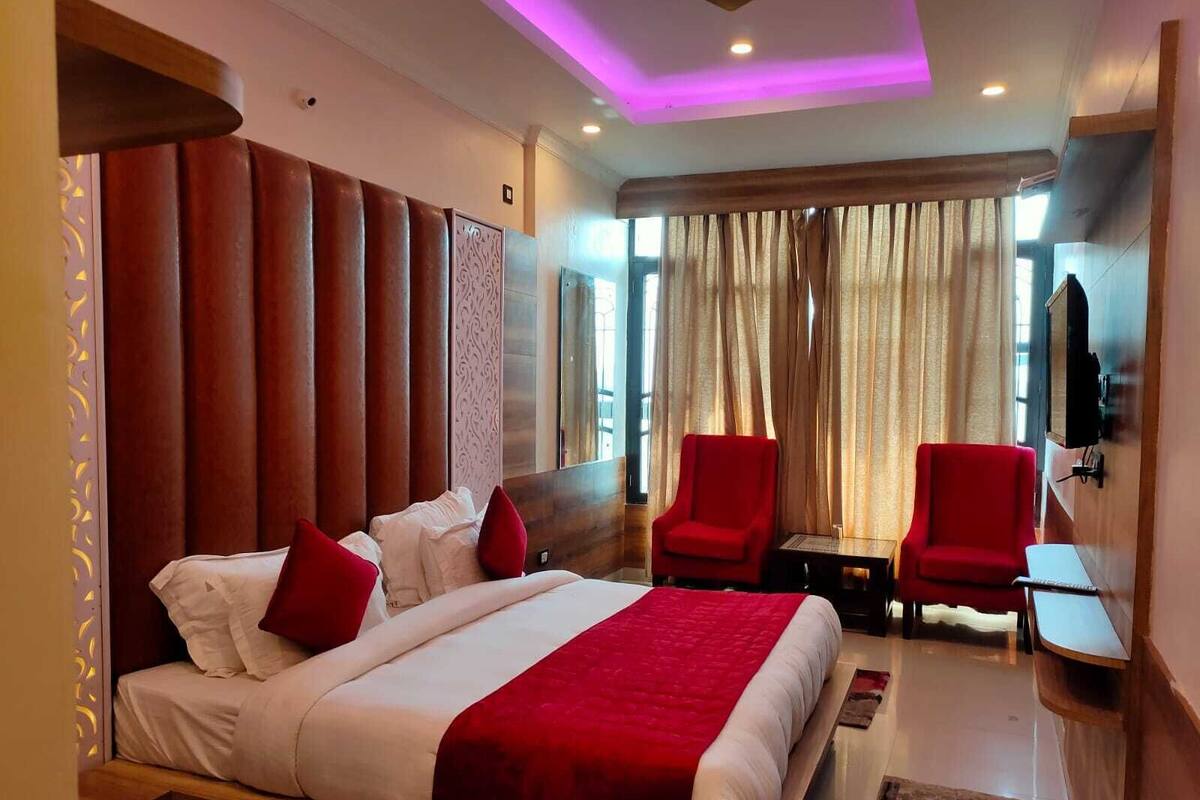 Ein Hotelzimmer mit einem großen Bett, zwei roten Sessel, einem kleinen Tisch und einem Fernseher.