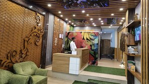 A reception area with a wooden reception desk, green upholstered chairs, and a television on the right. - Hotel Grand Hill (Dharamshala)