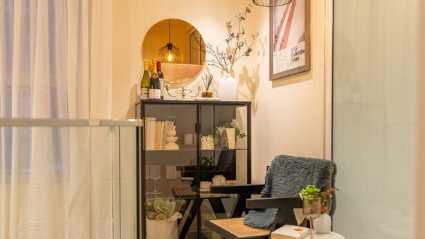 Una sala de estar moderna con un separador de vidrio, un sillón acogedor, una mesita redonda y un espejo decorativo.