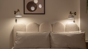 Un dormitorio con una cama, dos lámparas de pared y una obra de arte abstracta enmarcada sobre la cama.