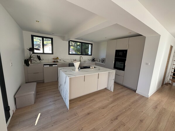 A modern kitchen with a marble island, built-in appliances, and large windows.