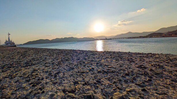A rocky beach with a ship in the background and mountains in the distance. - KULABO TAISHOKAN (Nagato)