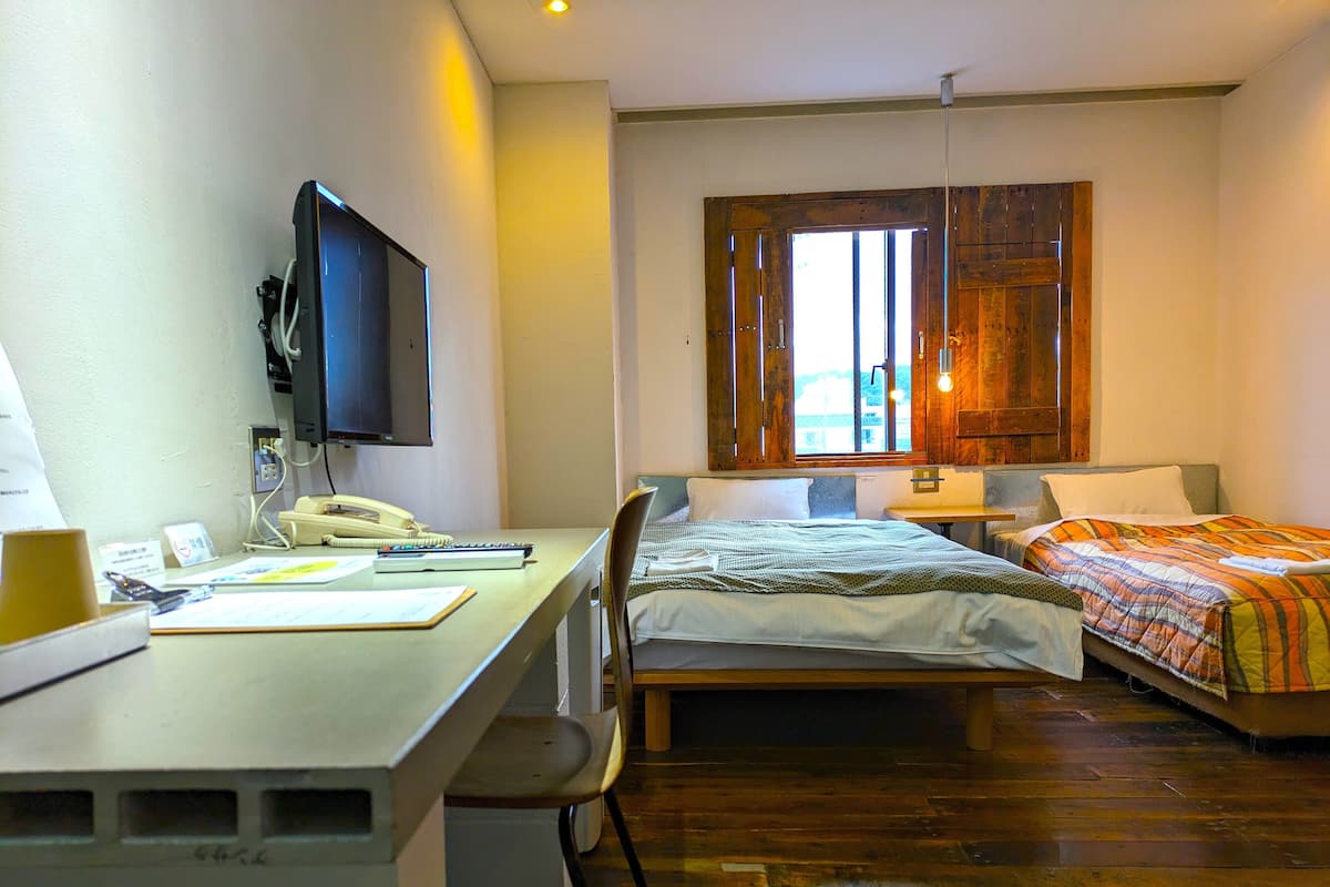 A hotel room with a desk, a bed, a TV, and a window with wooden shutters.