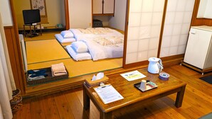 A traditional Japanese-style room with tatami flooring, a bed with white bedding, a wooden table with a teapot, and a small refrigerator. - KULABO TAISHOKAN (Nagato)