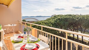 A balcony with a table set for dining, overlooking a body of water and a bridge.