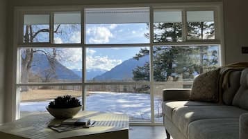 A room with a large window, a sofa, a table with a bowl, and a laptop.