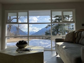 A room with a large window, a sofa, a table with a bowl, and a laptop. - Scenic Bluebird House with Mountain views, AC & Ho (Columbia Falls)