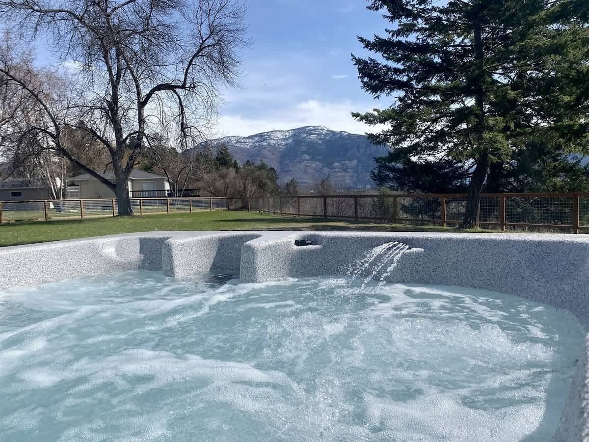 A hot tub with a mountainous backdrop, surrounded by a fenced area with trees.